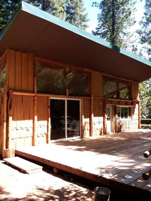 A wooden cabin with a deck, large sliding glass doors, and a covered porch.