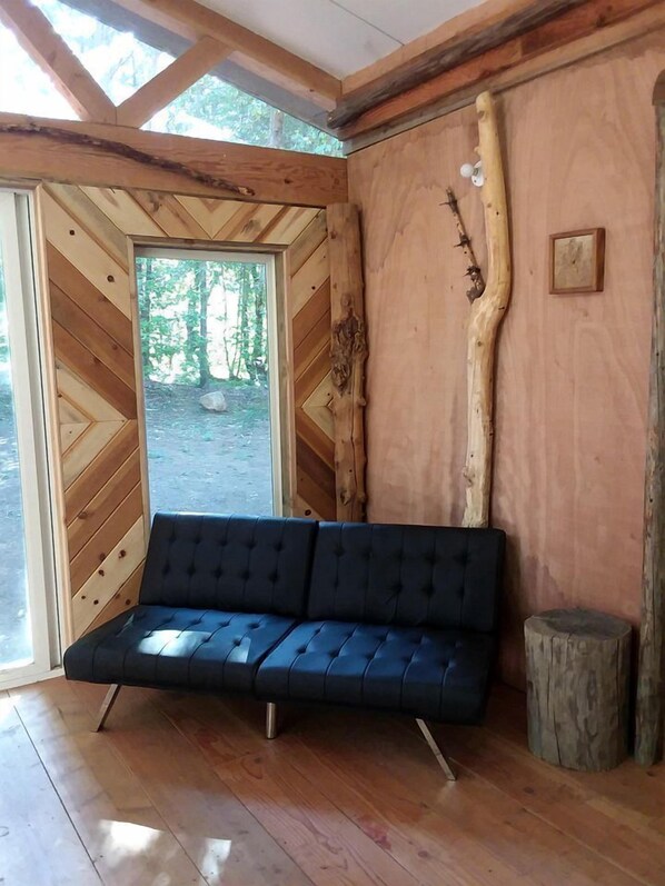 A wooden interior with a sofa, a wooden wall with a tree branch, and a door leading outside.