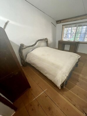 A single bed with a wooden headboard in a room with wooden flooring and a window.