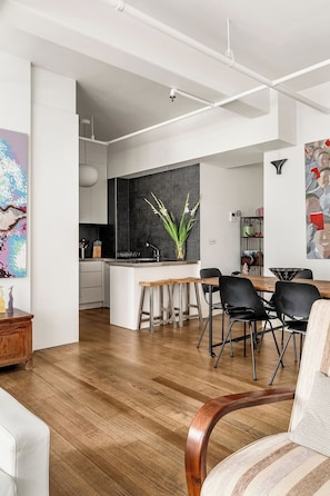 A modern kitchen with a black backsplash, wooden bar stools, and a dining area with black chairs. - Luxury Villas The Lane Hideaway (Melbourne)