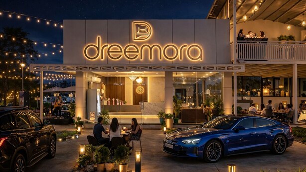 En modern byggnad med en neonskylt som visar ordet ”dreamora”, uteservering och en blå bil parkerad framför.