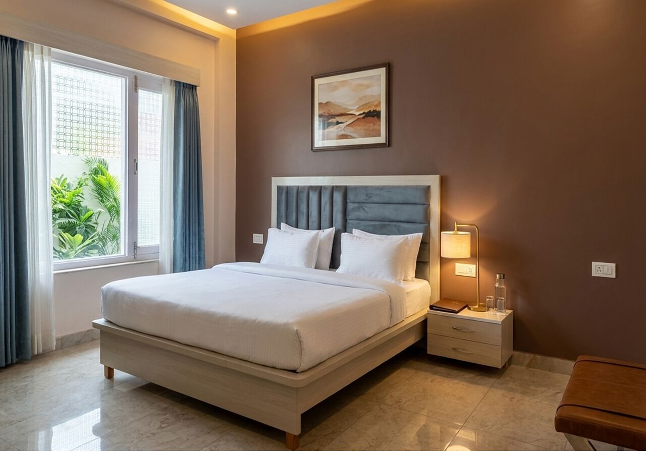A hotel room with a bed, bedside table, lamp, and a painting on the wall.