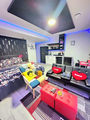 A modern living room with a sofa, a red ottoman, a coffee table, and a TV. - Swithome Properties Cozy Studio Pond View, Near Yeg Airport (Edmonton)