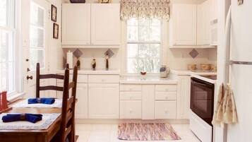 A kitchen with white cabinets, a dining table with blue placemats, a window with lace curtains, and a kitchen island with a microwave.
