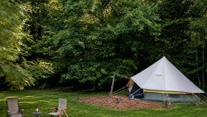 A tent set up in a grassy area with two chairs and a fire pit nearby. - Off-Grid Creekside Tent Ideal for a Glamping Experience in Cosby, Tennessee (Cosby)