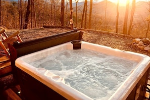 A hot tub with a wooden deck and a view of a forest and mountains.