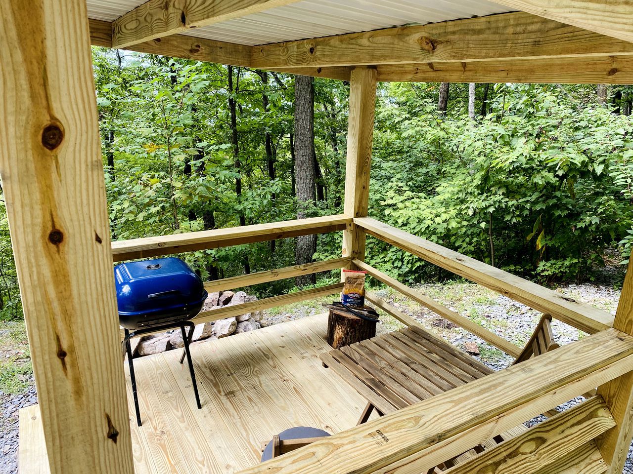 A wooden deck with a barbecue grill, a bag of charcoal, and a small table.