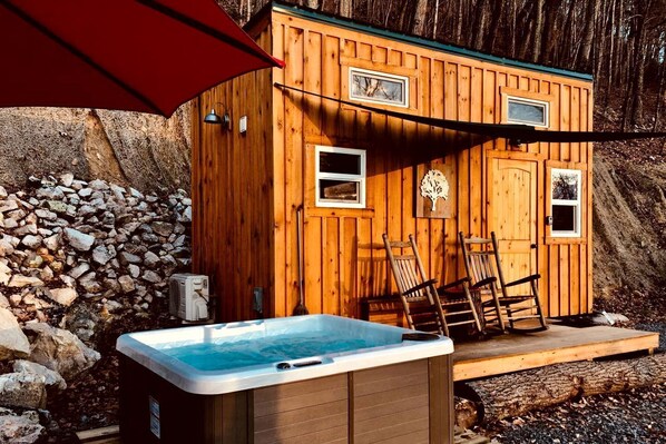 A wooden cabin with a hot tub, two windows, and a stone wall.