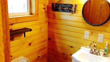 A wooden cabin bathroom with a toilet, sink, window, and a mirror.