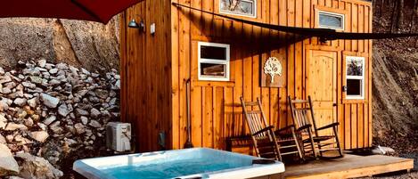 A wooden cabin with a hot tub, two windows, and a stone wall.