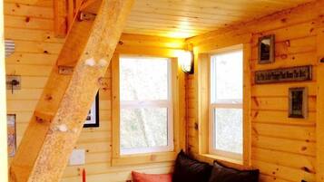 A cabin interior with a wooden staircase, a sofa, a small table, and two windows.