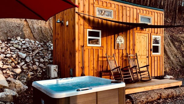 A wooden cabin with a hot tub, two windows, and a stone wall. - Unique Wooden Tennessee Cabin near Knoxville for Relaxing Great Smoky Vacations (Newport)