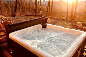 Ein Whirlpool mit einer Holzterrasse und Blick auf einen Wald und Berge.