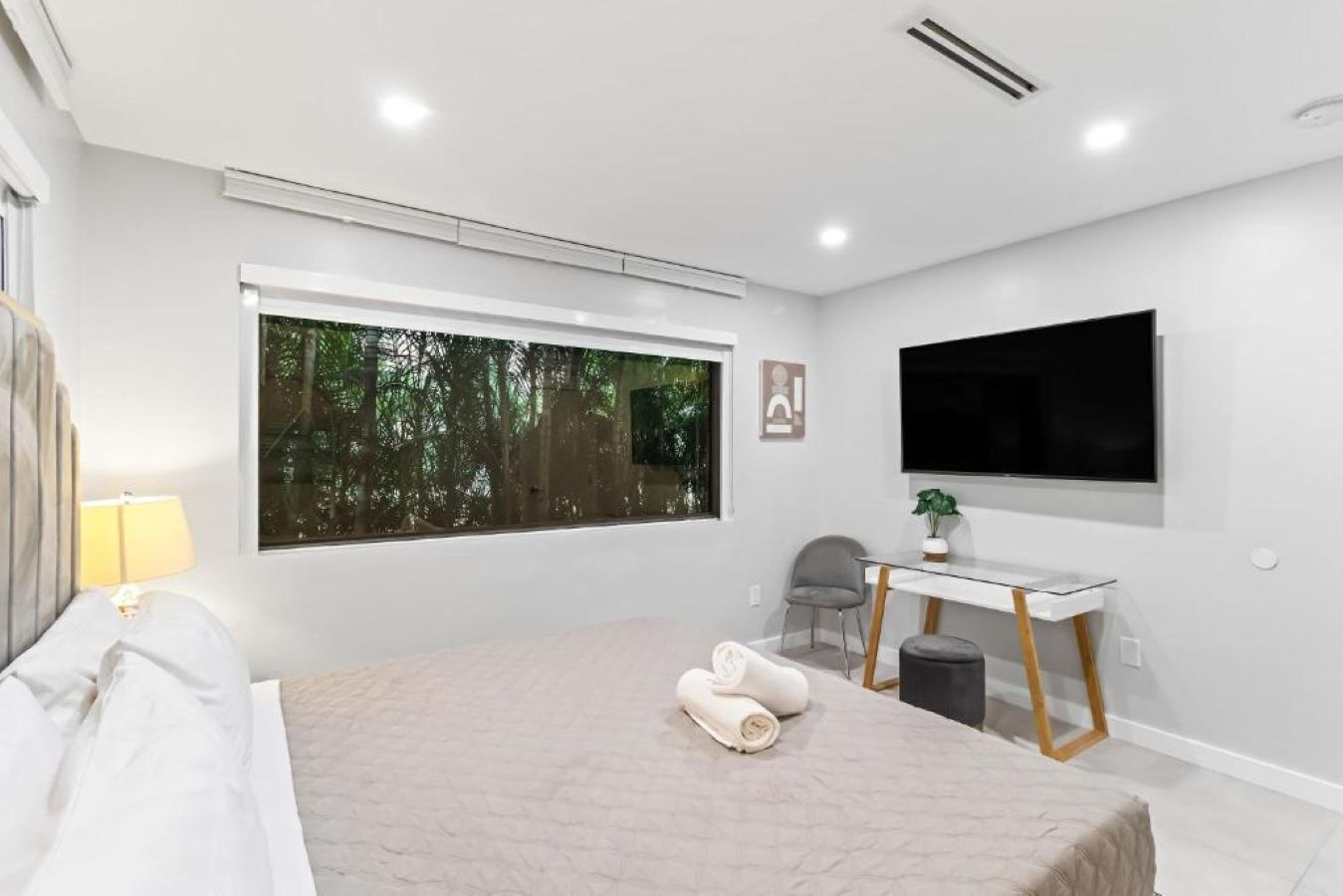 A modern bedroom with a large window, a bed, a desk, and a TV.