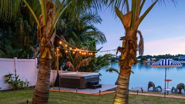 A backyard with a hot tub, palm trees, a pool, and string lights. - Lakefront Tropical Villa by Glam Homes  (North Miami Beach)