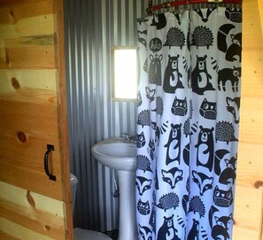 Ein Badezimmer mit Holzwand, Waschbecken in Weiß und einer Duschvorhang mit Tiermotiv.