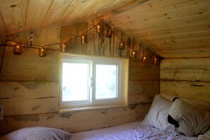 Ein Zimmer in einer Holzhütte mit Fenster, einem Bett und Lichterketten.