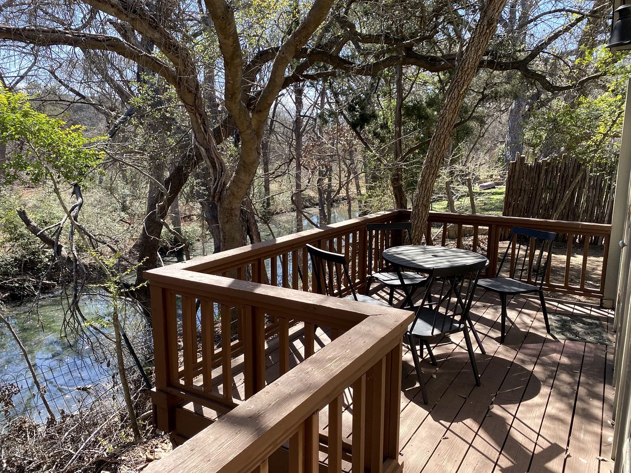 A wooden deck with a table and chairs, surrounded by trees and a body of water.