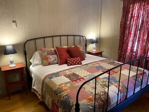 Um quarto com estrutura de cama em metal, colcha acolchoada, duas mesas de cabeceira com abajures e piso de madeira.