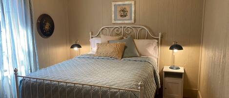 A bedroom with a bed, two bedside tables, a nightstand, a wall clock, and a window with curtains.