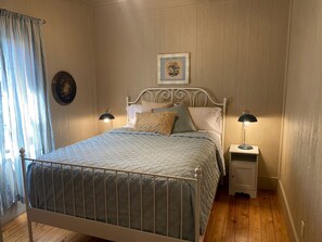 A bedroom with a bed, two bedside tables, a nightstand, a wall clock, and a window with curtains. - Elevate Your Holidays: Glamping at Cypress Creek Cottage, Texas' Hidden Gem (Wimberley)