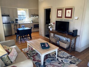 A modern kitchen with stainless steel appliances, a dining area with a table and chairs, a living room with a sofa and a coffee table, and a flat-screen TV on a wooden stand. - Elevate Your Holidays: Glamping at Cypress Creek Cottage, Texas' Hidden Gem (Wimberley)