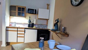 Une cuisine avec une table en bois, des assiettes, des tasses et une horloge au mur.