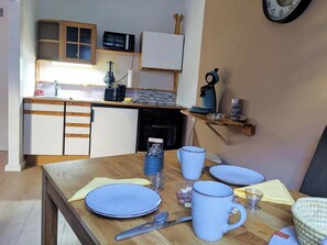 A kitchen with a wooden table, plates, mugs, and a clock on the wall. - Holiday apartment Brunnenplatz in our guesthouse in  old town of Zell (Moselle) (Zell (Mosel))
