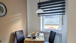 Un coin repas comprenant une table, des chaises, une horloge et une fenêtre avec des stores.