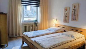 Un lit double avec une literie à rayures, une lampe de chevet, un radiateur et une fenêtre avec des rideaux.