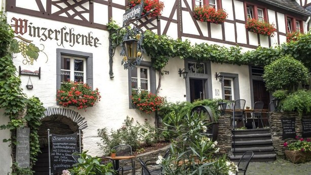Un bâtiment traditionnel à colombages, avec une enseigne indiquant « Winzerchenke », des places assises à l’extérieur et un escalier en pierre menant à l’entrée.
