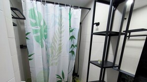 Un baño con inodoro, ducha con cortina de hoja de bambú, lavamanos con encimera de mármol y un estante negro.