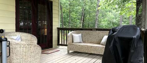 A covered porch with wicker furniture, a grill, and a view of trees.