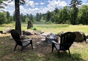 Two Adirondack chairs facing a campfire in a forested area with a clear sky. - Cozy Cabin Rental near Ozark National Forest for a Relaxing Weekend Getaway in Arkansas (Harrison)