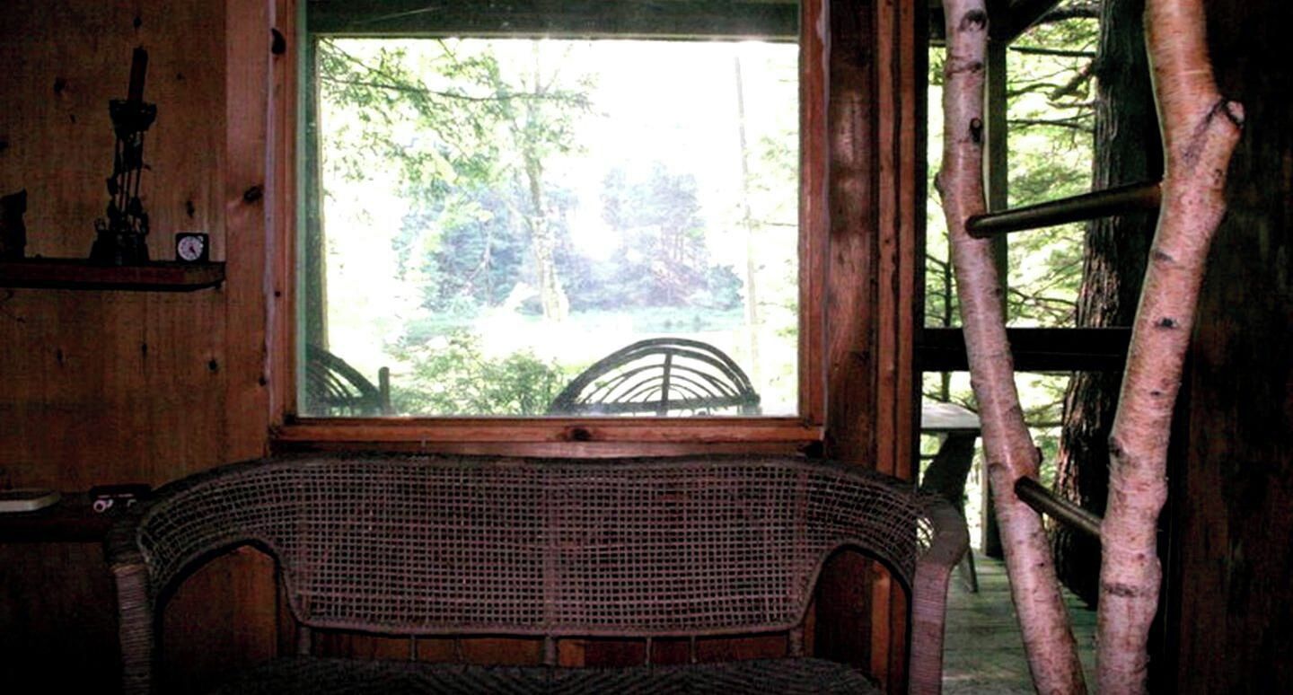 A wicker chair in front of a window with a view of trees.