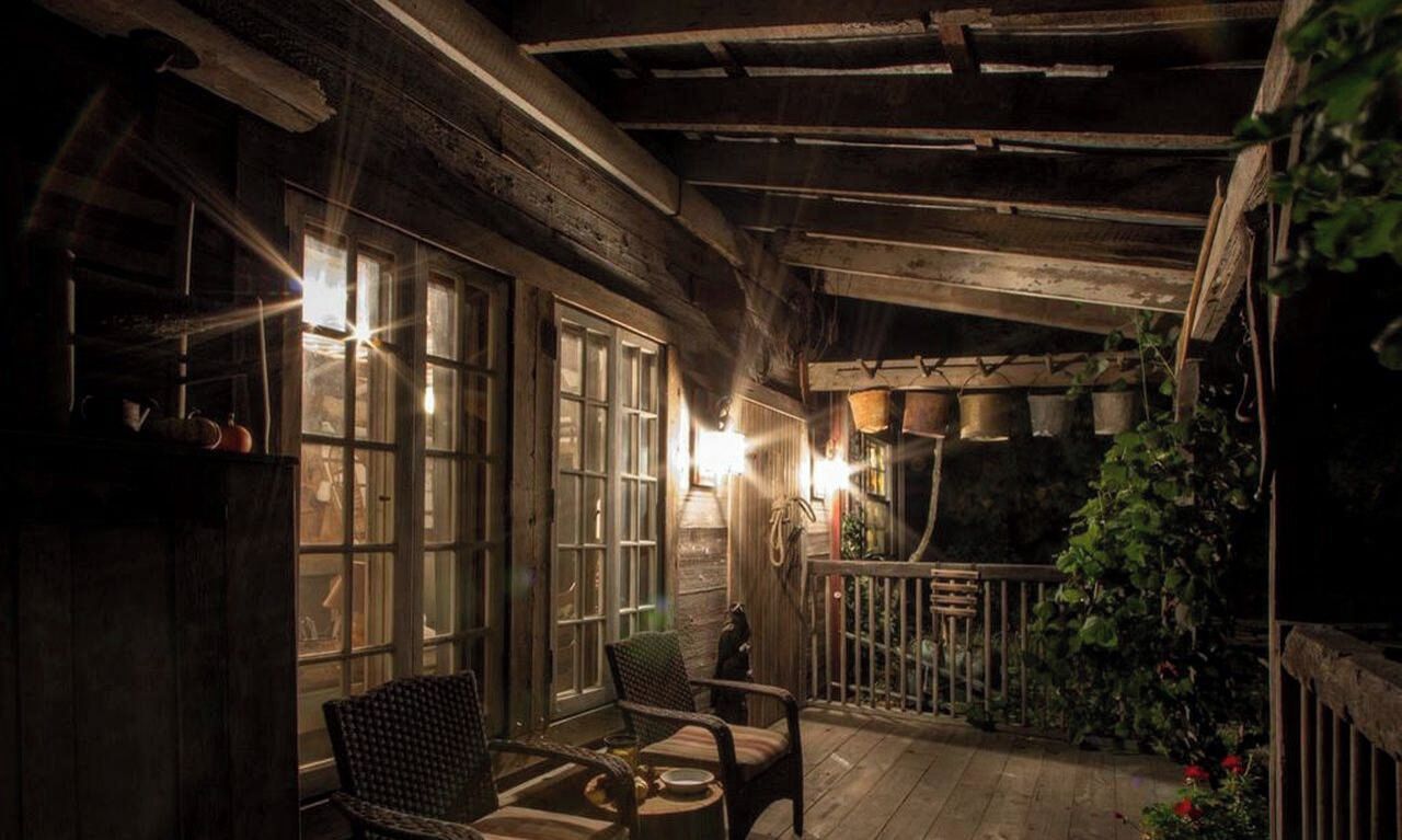 Un portico in legno con una sedia e un tavolo, un muro in pietra con piante in vaso e una ringhiera di legno.