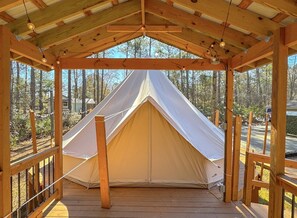 A wooden pavilion with a tent in the center, surrounded by a wooden deck and railings.