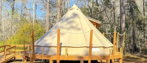 A dome-shaped tent with a wooden frame and a platform, surrounded by trees.