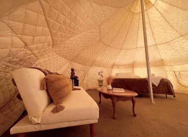 A tent with a cushioned seating area, a small table, and a bed.