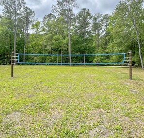 A volleyball net in an open grassy area surrounded by trees. - Cozy Glamping Tent with Rain Shower in Calabash, North Carolina (Calabash)