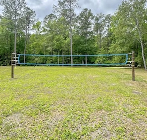 Ein Volleyballnetz in einer offenen, grünen Lichtung, umgeben von Bäumen.