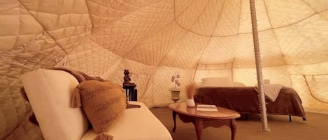 A tent with a cushioned seating area, a small table, and a bed.