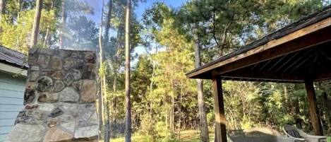 Une cheminée en pierre, des sièges d’extérieur et un paysage boisé en arrière-plan.