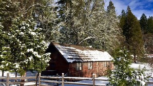 Una cabaña rústica con techo inclinado, rodeada de árboles cubiertos de nieve y una valla de madera.