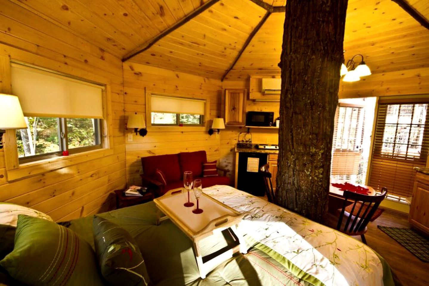 A cozy cabin with a wooden interior, a dining area, and a large tree trunk in the center.