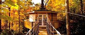 Een houten boomhut met een touwbrug, omringd door herfstbladeren.