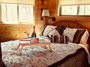 Een houten kamer met een bed, een nachtkastje met een dienblad, een fles en glazen.
