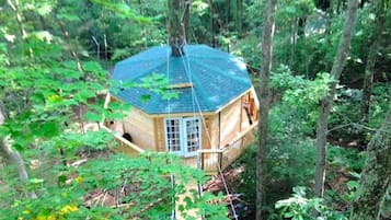 Ein Baumhaus mit einem Sechseckgrundriss, umgeben von dichtem Wald.