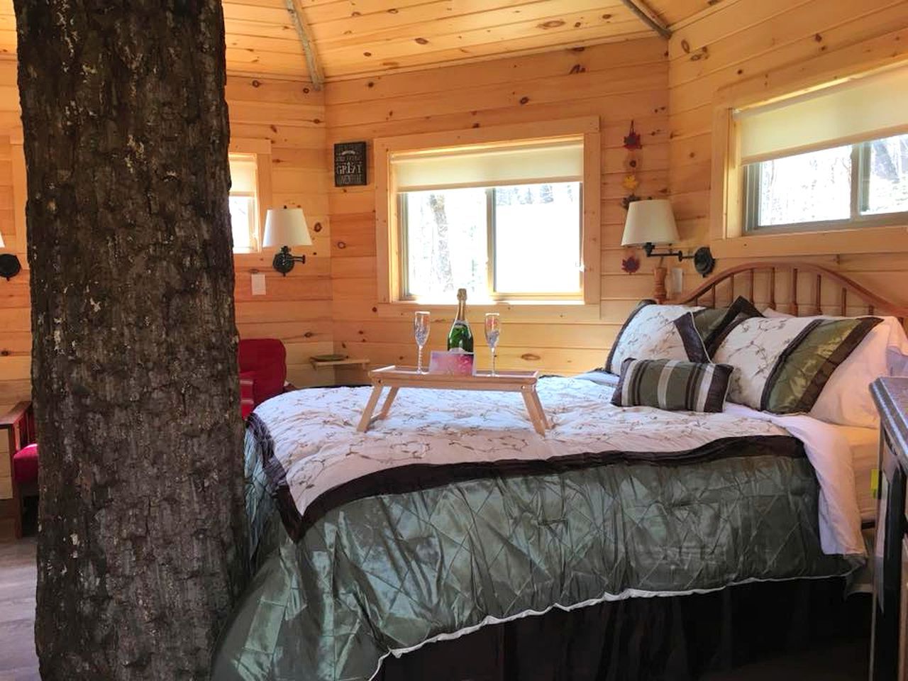 Un dormitorio de cabaña de madera con cama, mesita de noche, ventana y tronco de árbol.