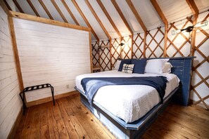 Une chambre avec un plafond en bois, un lit avec une literie blanche, un plancher en bois et un petit banc en métal.